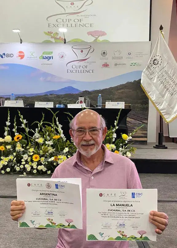 Photo of man showing awards of coffee cup of excelence in El Salvador