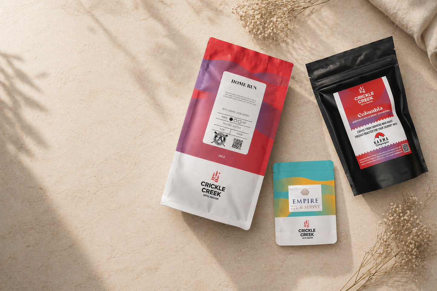 Three custom specialty coffee packages from Crickle Creek on a beige surface with dried plants.