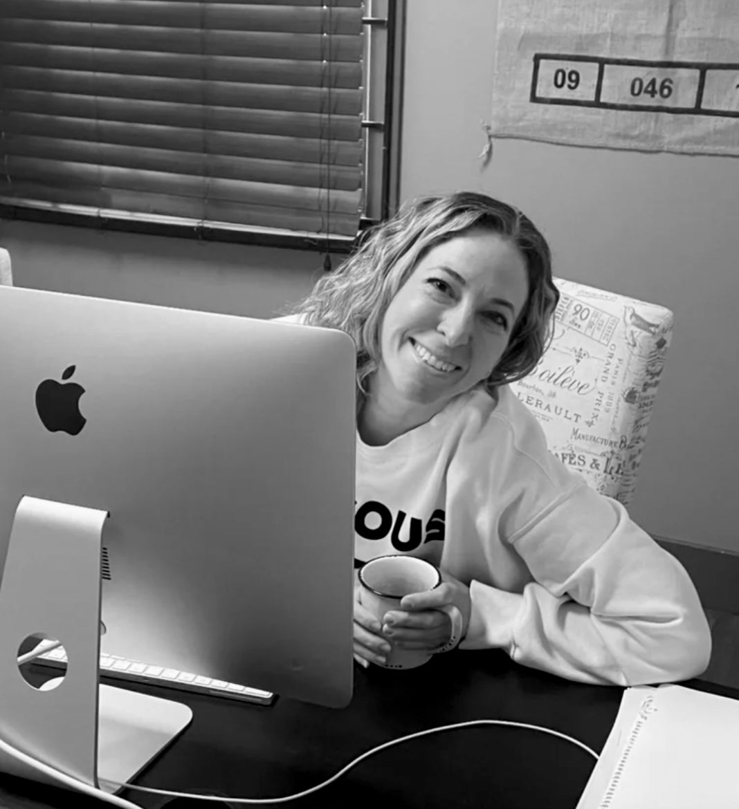 Person sitting at a desk with a computer and a cup, smiling.