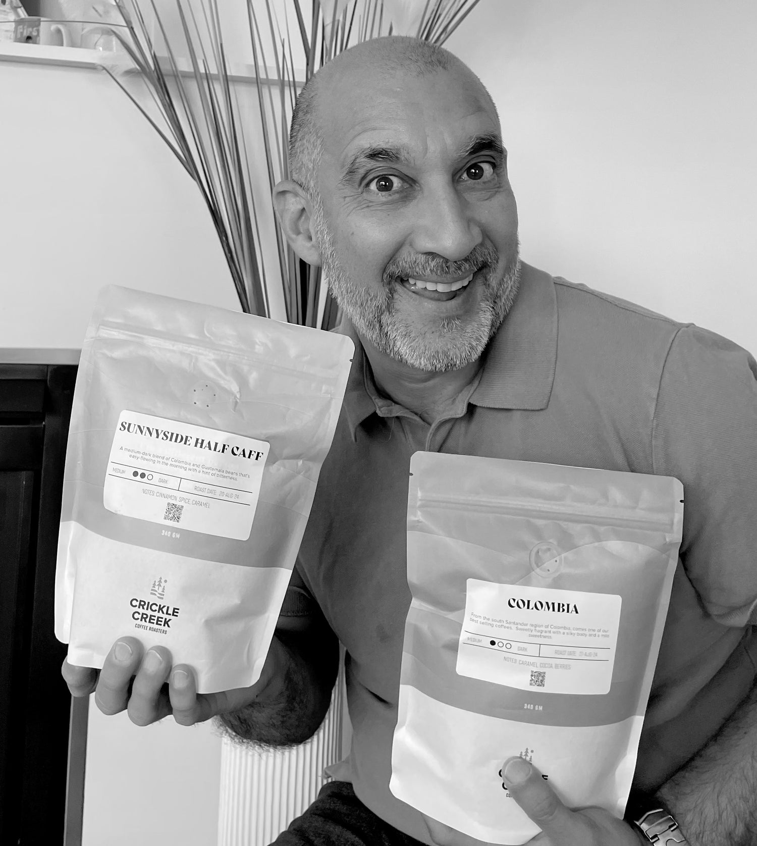 Man holding two packages of Crickle Creek coffee, with a neutral background