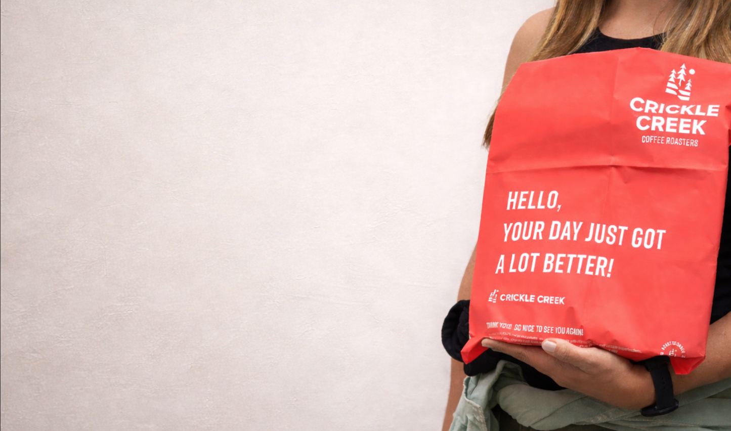 Person holding a red Crickle Creek bag with text on a plain background