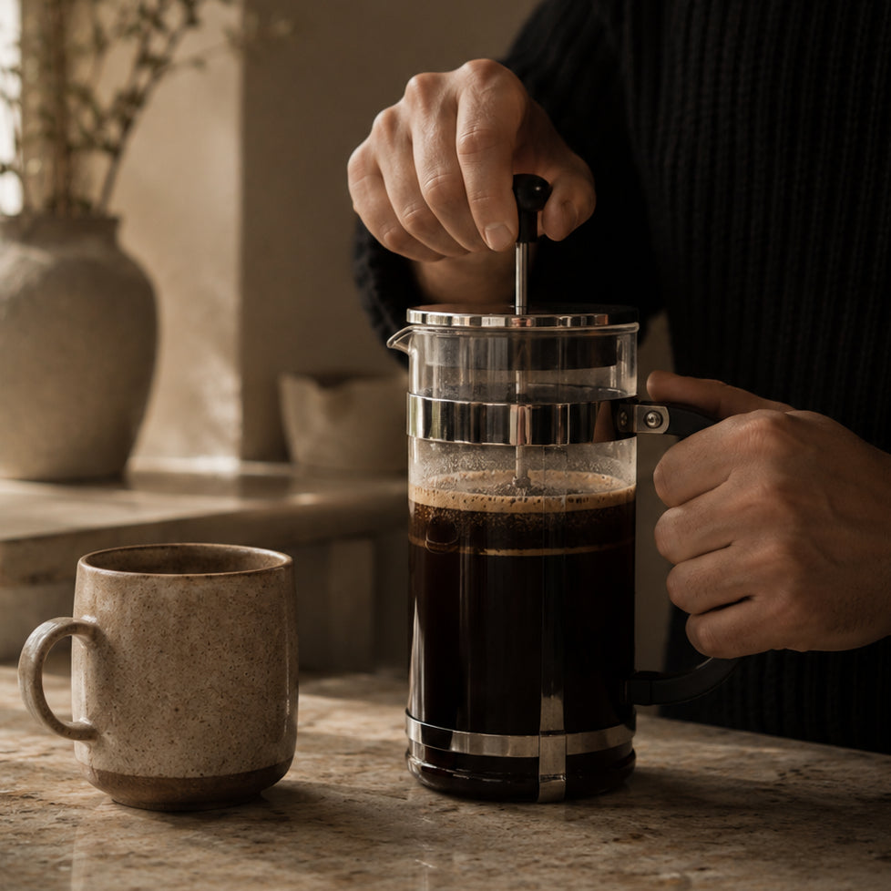 Person making coffee using a French press with the best coffee beans in Canada on a wooden table.