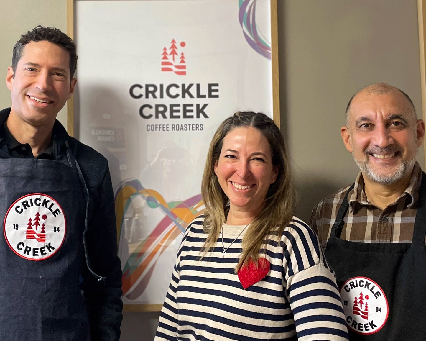 Three people wearing aprons with 'Crickle Creek' branding in a casual setting.